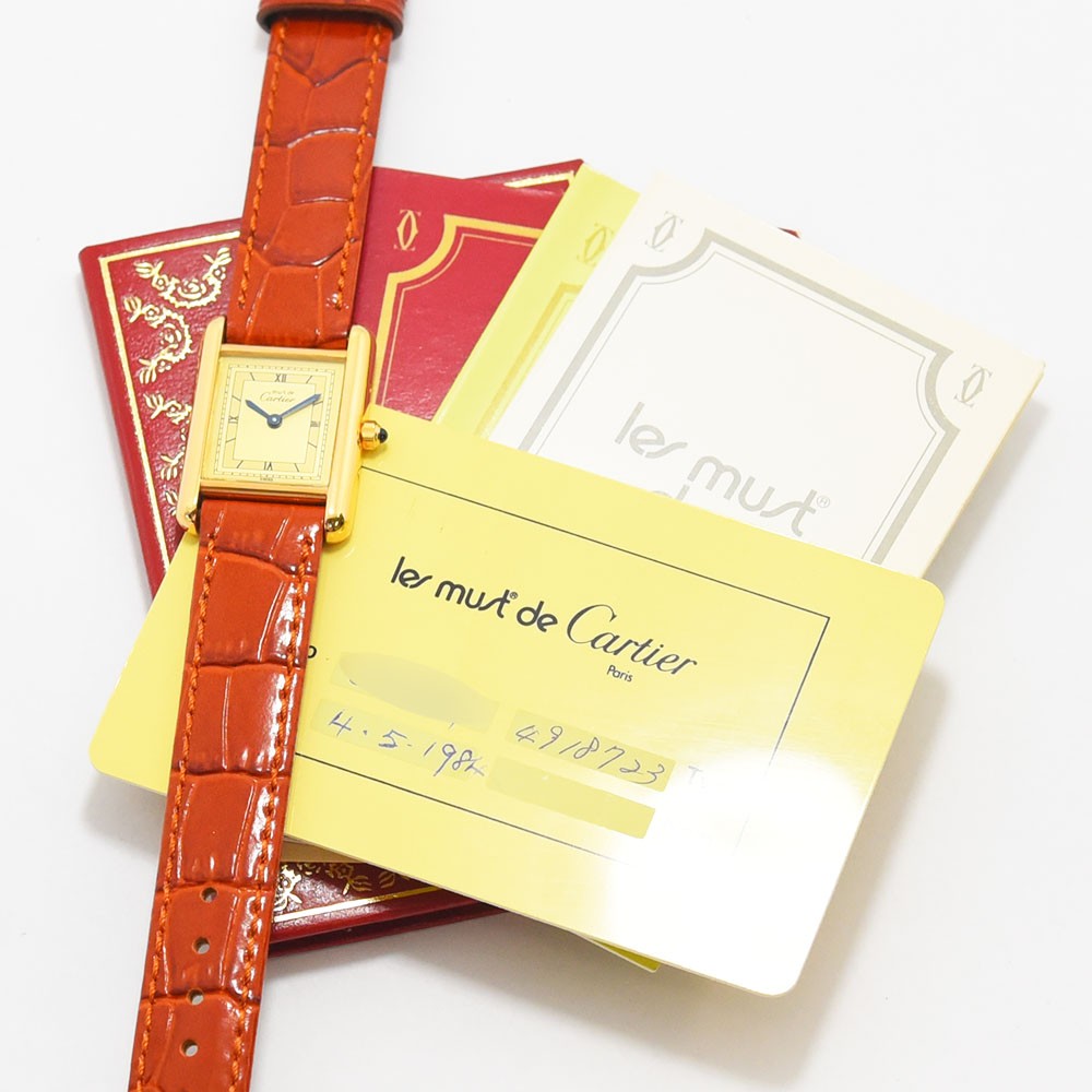 VINTAGE WATCHES FASHIONのMust de Cartier Tankウォッチ、ゴールドトーンケース、クリーム色の文字盤、ローマ数字、オレンジのアリゲーター型押しレザーストラップ。